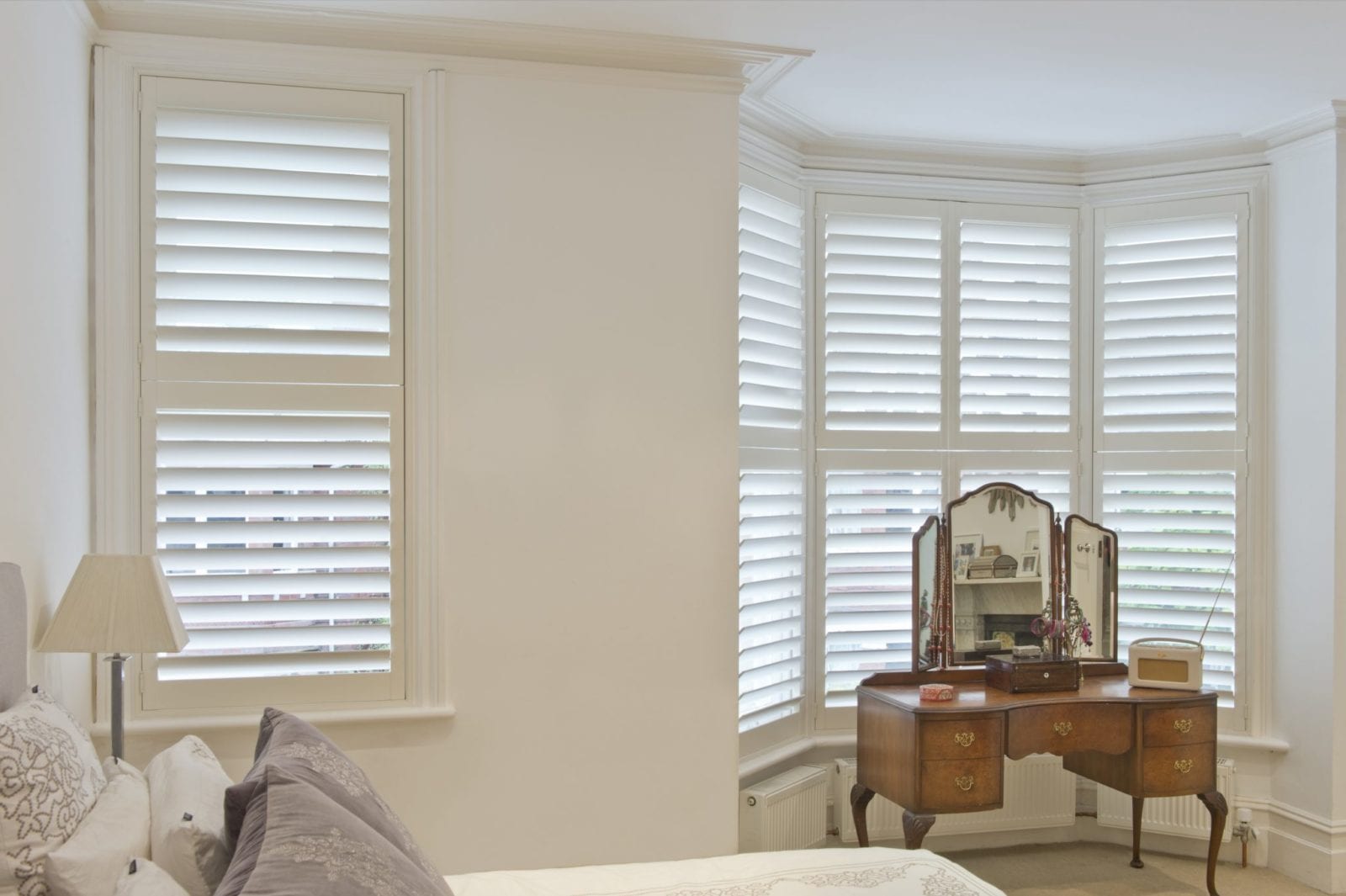 White shutters on a bedroom bay window beside a dressing table with a mirror