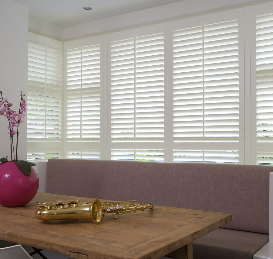 White plantation shutters across a wide living room window above a wooden coffee table