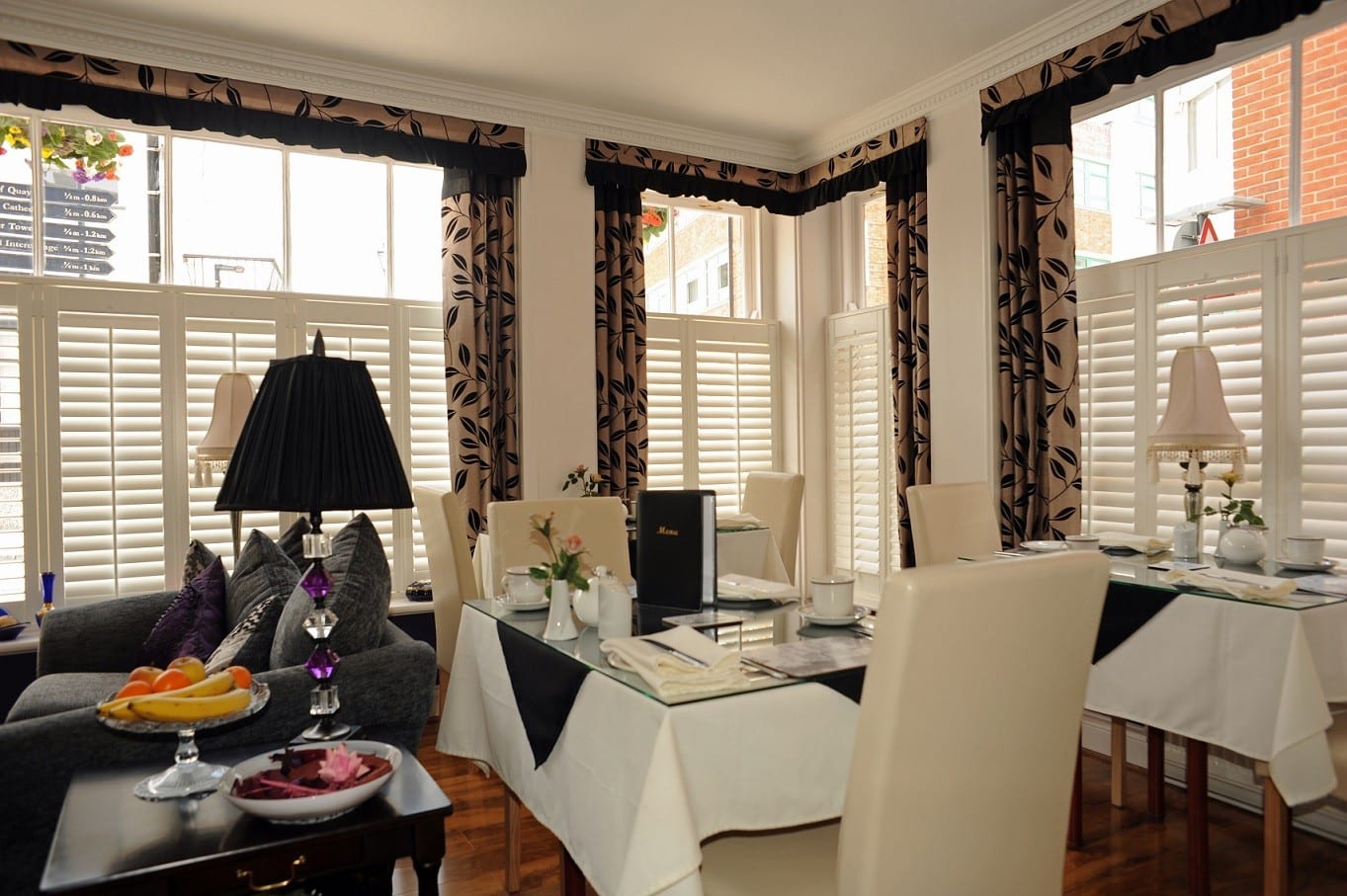 Café style shutters on tall windows framed by dark patterned curtains in a dining room