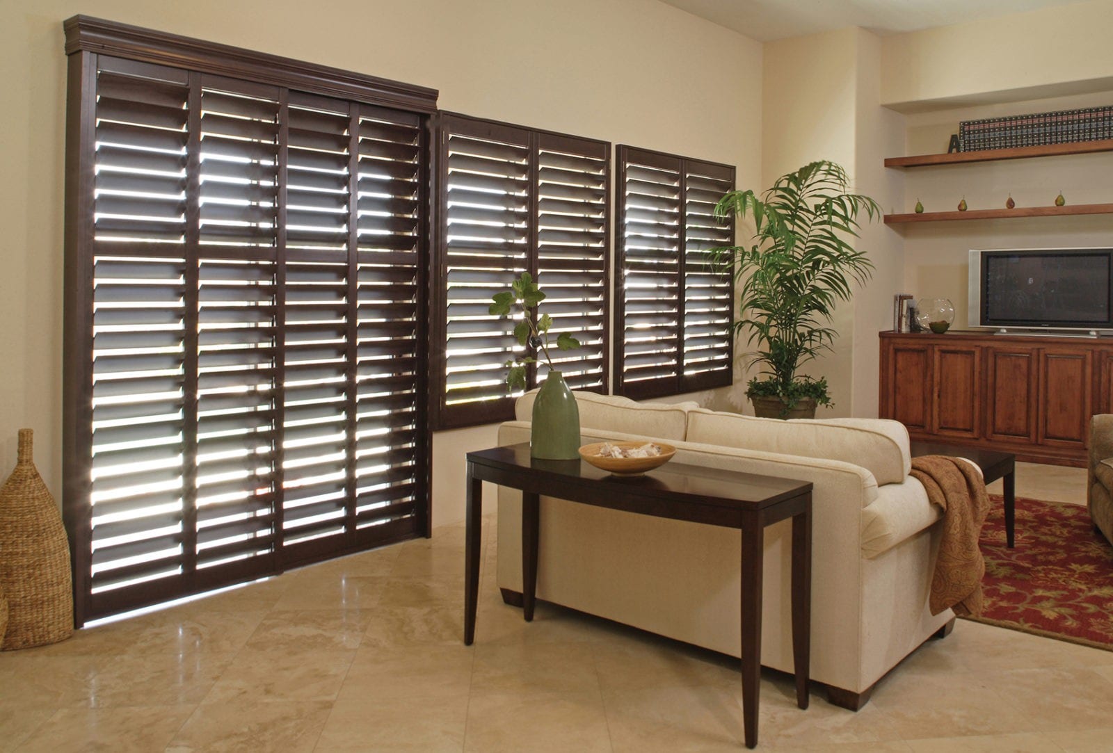 Dark wood tracked shutters in a lounge with a sofa and console table