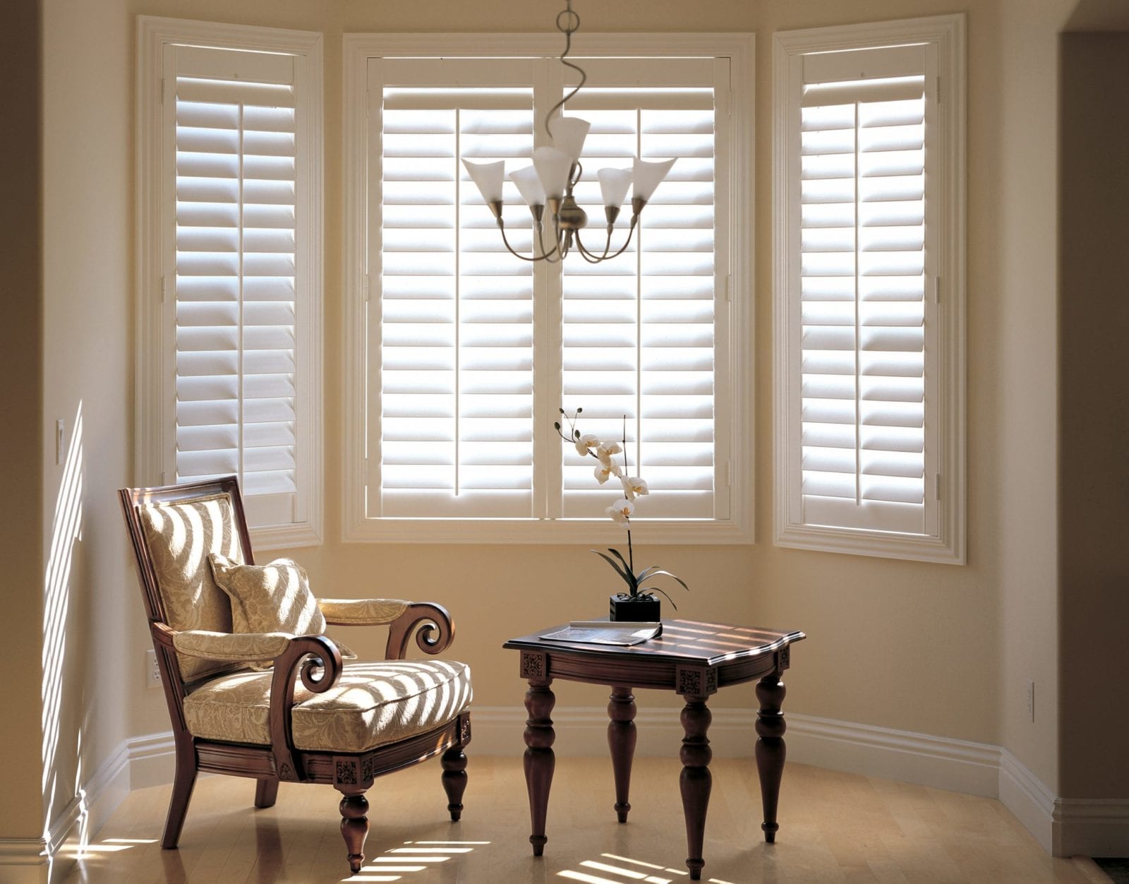 White bay window shutters in a cream living room with a striped armchair and side table