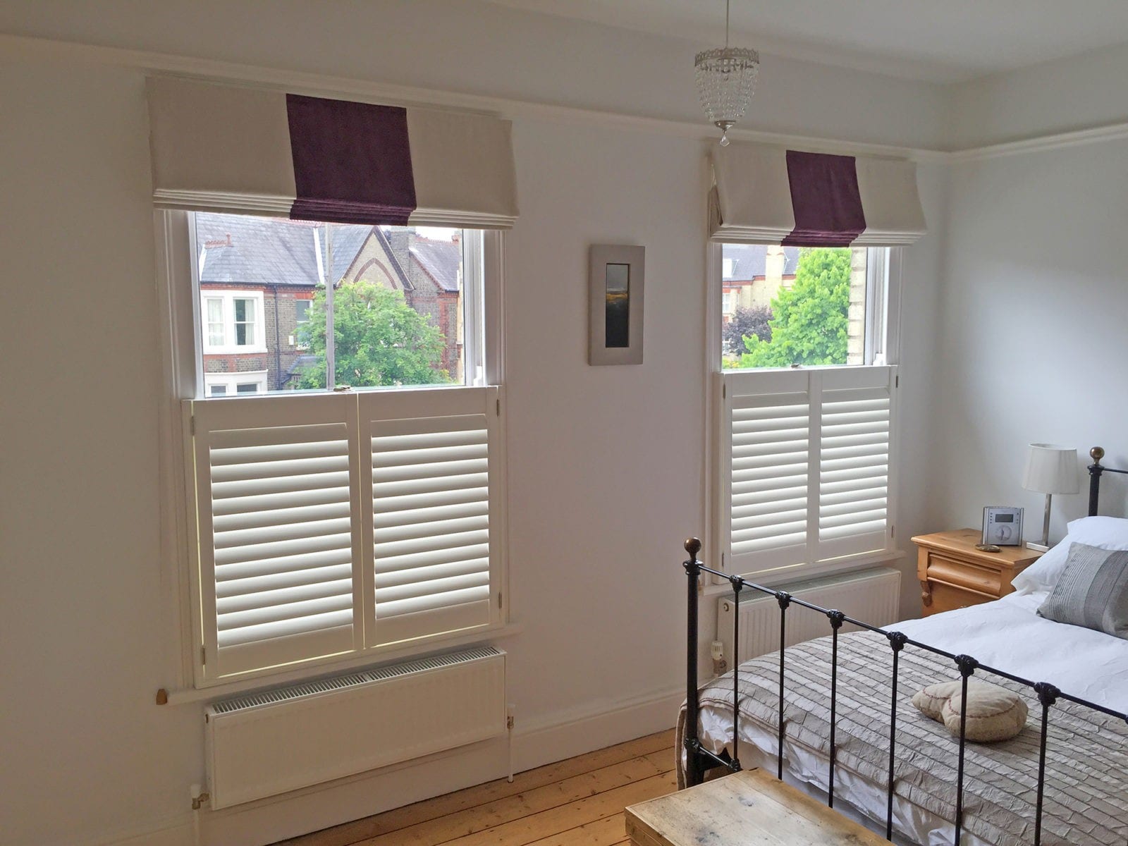 Café style shutters on bedroom windows above a wrought iron bed