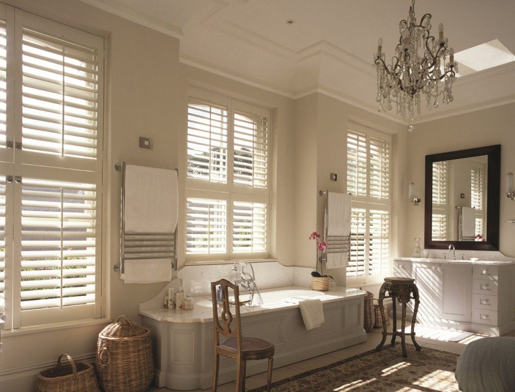 Tier on tier shutters in a bathroom with a freestanding bath and chandelier