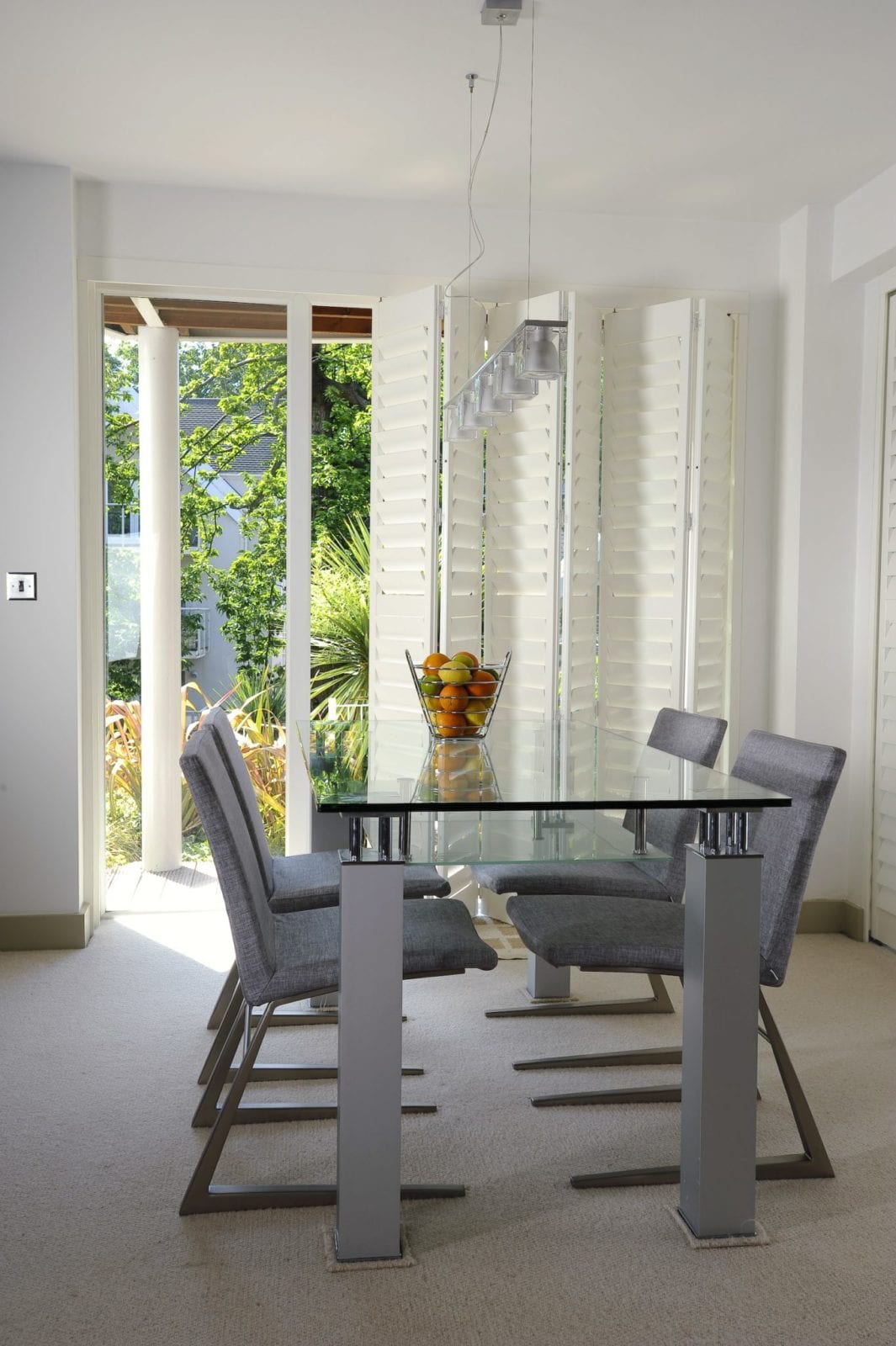 White tracked shutters beside glazed doors in a bright dining area