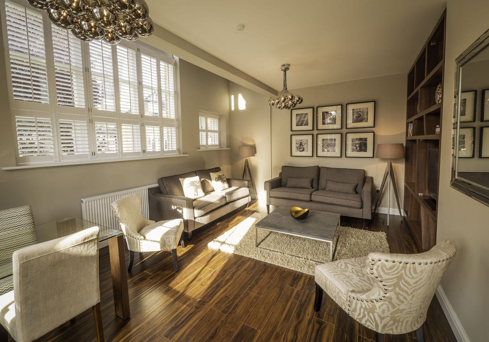 Living room with shutters on a tall window, cream sofas and a dark wood floor