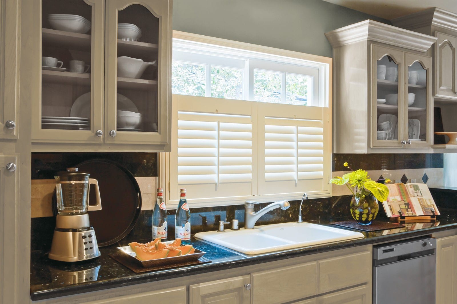 Café style shutters over a kitchen sink window with dresser cabinets either side