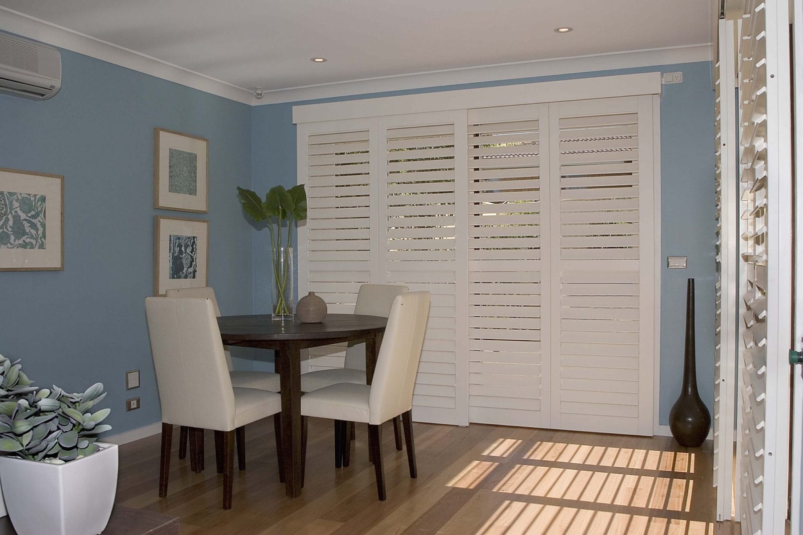 White tracked shutter panels on a dining room wall with blue walls and a table with chairs