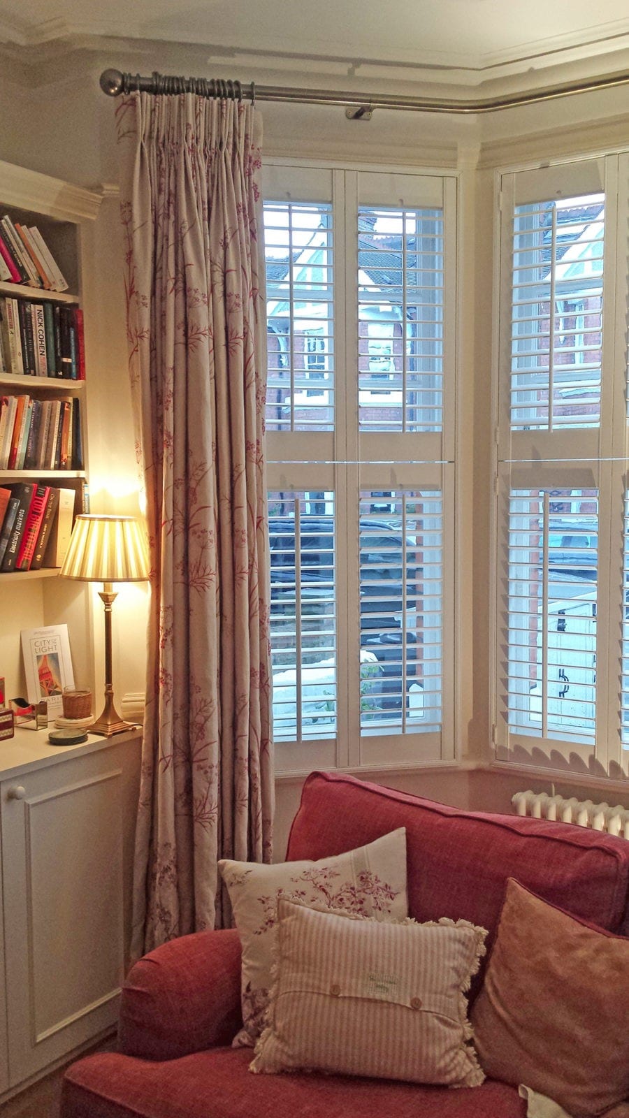 Tier on tier shutters on a bay window alongside patterned curtains