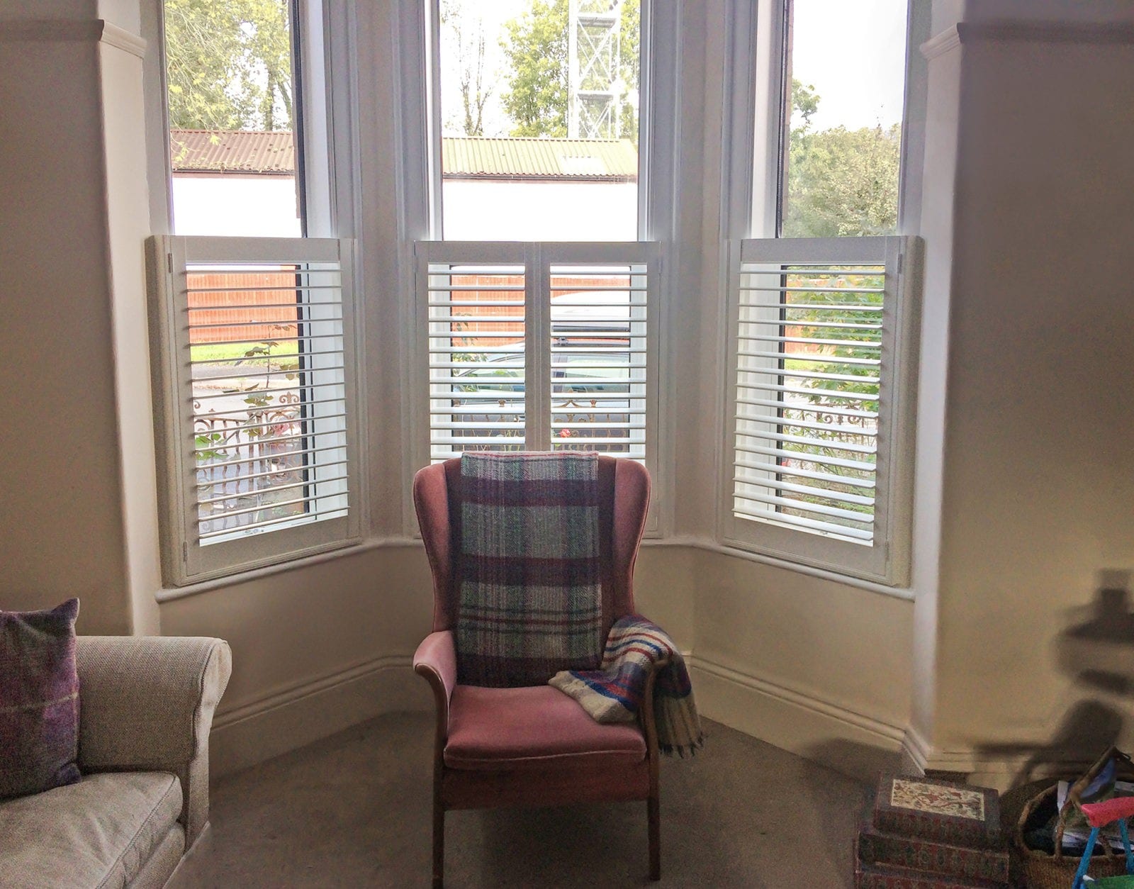 Café style shutters on a bay window with a red armchair