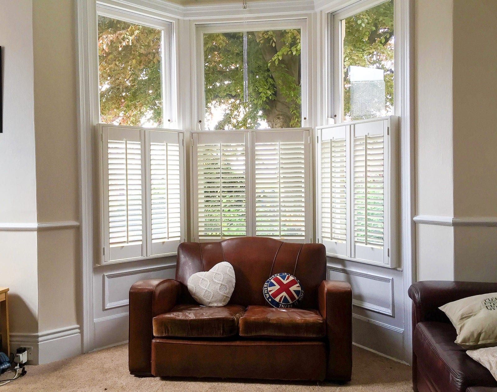 Café style shutters on a bay window above a brown leather armchair